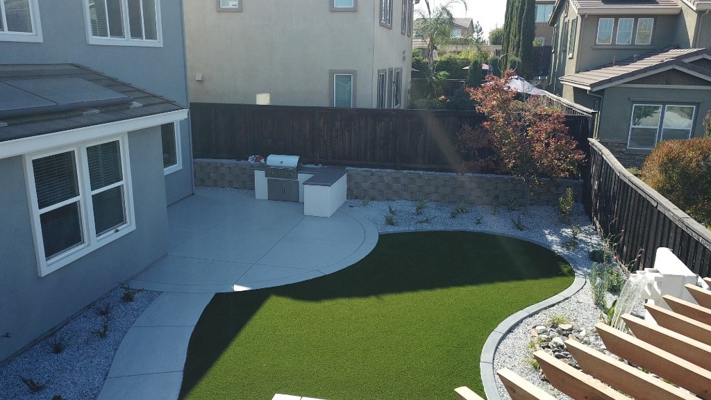 Backyard with curved concrete patio, artificial turf, built-in BBQ and stone retaining wall