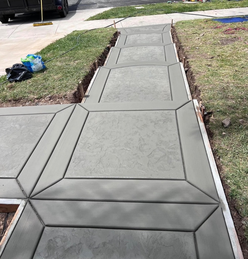 Freshly stamped concrete walkway under construction with geometric pattern